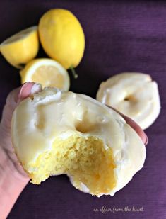 a person holding a half eaten doughnut with icing and lemons in the background