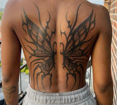 a man with tattoos on his back standing next to a brick wall