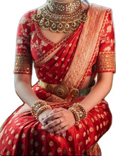 a woman in a red and gold sari with jewelry on her neck, sitting down