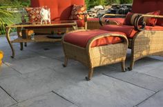 two wicker chairs and a footstool are sitting on a patio with red cushions