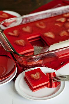 strawberry jello is served on a plate with a fork and glass container in the background