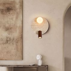 a white vase sitting on top of a table next to a wall mounted light fixture