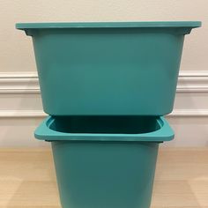 two green plastic containers sitting on top of a wooden table next to a wall and floor