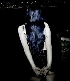 a woman with long blue hair standing in the dark