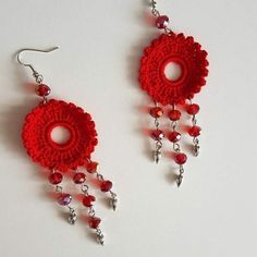 two red crocheted earrings with dangling chains and beads hanging from them on a white surface