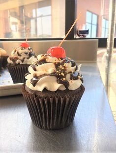 two cupcakes with chocolate frosting and cherries on top sitting on a table