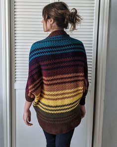 a woman standing in front of a door wearing a multicolored sweater