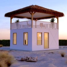 a small white house with a thatched roof on the beach at sunset or dawn