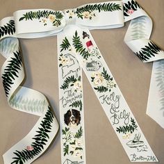 the ribbon is white with green leaves and flowers on it, along with other ribbons