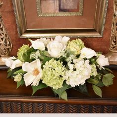 a bouquet of white and green flowers sitting on top of a wooden table next to a painting