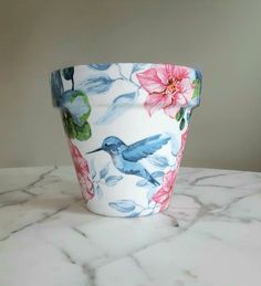 a cup with flowers painted on it sitting on a marble countertop next to a wall