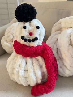 two knitted snowmen sitting next to each other on a couch, one wearing a red scarf