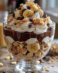 a dessert in a glass bowl on top of a table with nuts and chocolate toppings