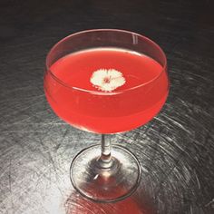 a red drink sitting on top of a table next to a glass filled with liquid