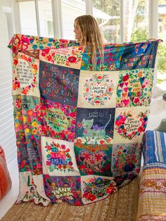 a woman holding up a colorful quilt on top of a bed next to a window