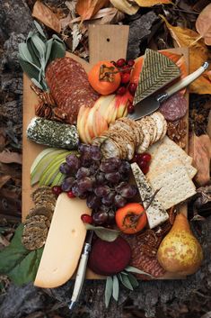 an assortment of cheeses, fruits and vegetables on a cutting board surrounded by leaves