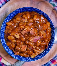 a blue bowl filled with beans and meat on top of a wooden plate next to a knife