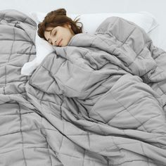 a woman laying in bed under a gray comforter and white pillow with her eyes closed