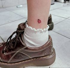 a ladybug tattoo on the ankle of a person wearing brown shoes and socks