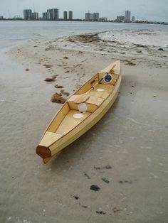 a small wooden boat sitting on top of a sandy beach next to the ocean with buildings in the background