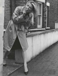 a black and white photo of a woman leaning against a wall talking on a cell phone