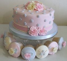 there is a pink cake with flowers on the top and other decorations around it, along with cupcakes