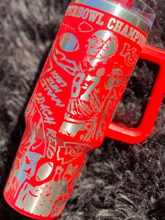 a red and silver travel mug sitting on top of a pile of black fur covered ground