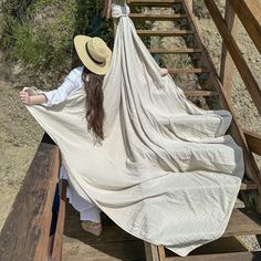 a woman sitting on top of a wooden bench covered in a white blanket and hat