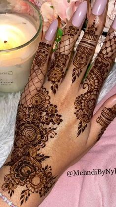 a woman's hand with henna on it next to a candle and flowers