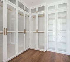 a white closet with glass doors and gold handles in a room that has wood floors