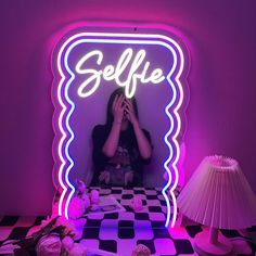 a woman taking a selfie in front of a neon sign with her hands to her face