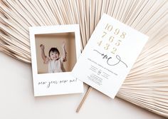 a white photo frame with gold numbers on it next to a palm frondy fan