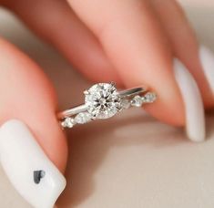 a woman's hand holding a diamond ring on top of her finger with white nail polish