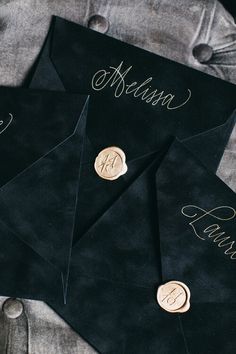 three black envelopes with gold buttons and names on them, sitting next to each other