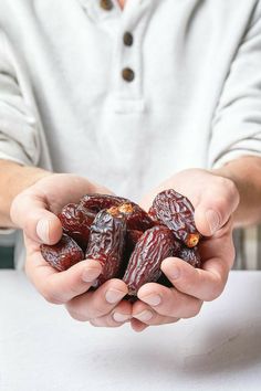 a person holding some kind of fruit in their hands on a white tableclothed surface