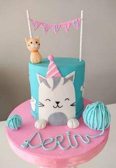 a birthday cake decorated with a cat and yarn ball on the top is blue and pink