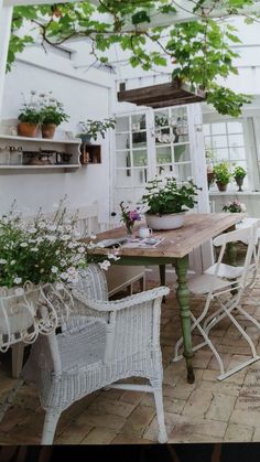 an outdoor dining area with white wicker chairs and wooden table surrounded by potted plants