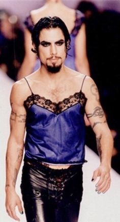 a man with tattoos on his arm walking down a runway wearing leather pants and a blue top