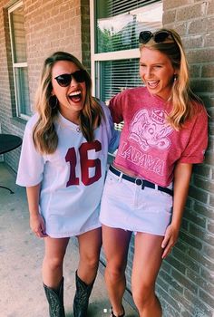 two women standing next to each other near a brick wall