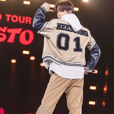 a male in a tan jacket and khaki pants standing on stage with his hands up