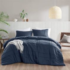 a bed with blue comforter and pillows in a room next to a plant on the floor