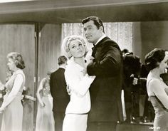 an old black and white photo of two people in formal wear dancing together with others