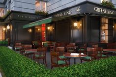 the outside of a restaurant with tables, chairs and green plants growing on the sidewalk