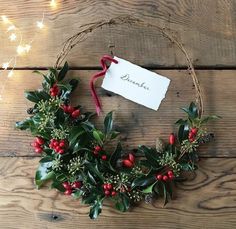 a christmas wreath with holly and berries hanging on a wooden wall next to a sign