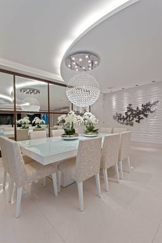 a dining room table with white chairs and chandelier hanging from it's ceiling