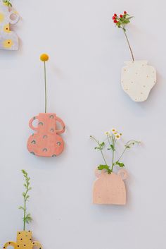 four flower vases are hanging on the wall with flowers in them, and one is made out of clay