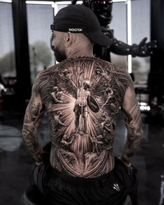 a man with tattoos on his back standing in front of a machine and looking at the camera