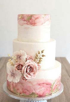 a three tiered cake with pink flowers on the top and white frosting on the bottom