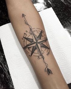 a black and white compass tattoo on the left arm with an arrow at the center