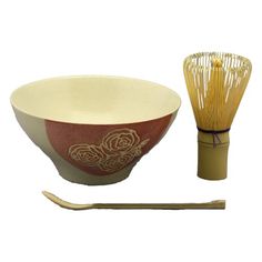 a red and white bowl next to a bamboo whisk on a white background